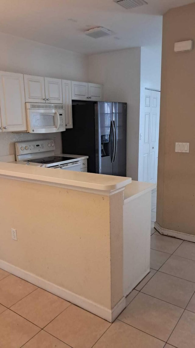 kitchen with kitchen peninsula, light tile patterned floors, white appliances, and white cabinetry