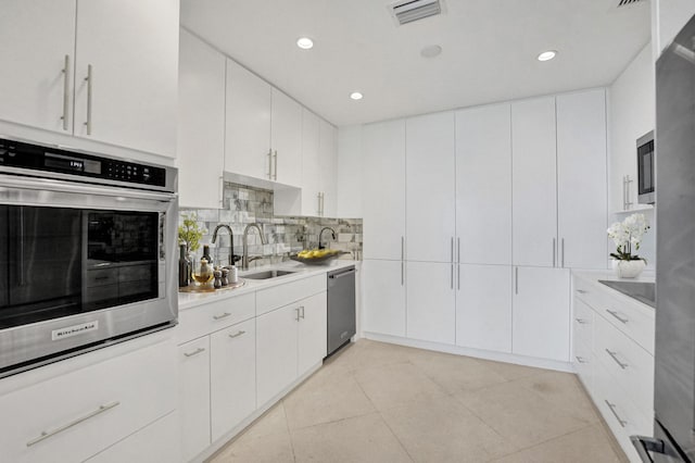 kitchen featuring white cabinetry, sink, stainless steel appliances, decorative backsplash, and light tile patterned flooring