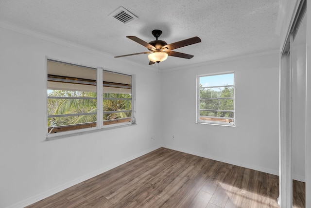 empty room featuring a textured ceiling, dark wood-type flooring, visible vents, and crown molding