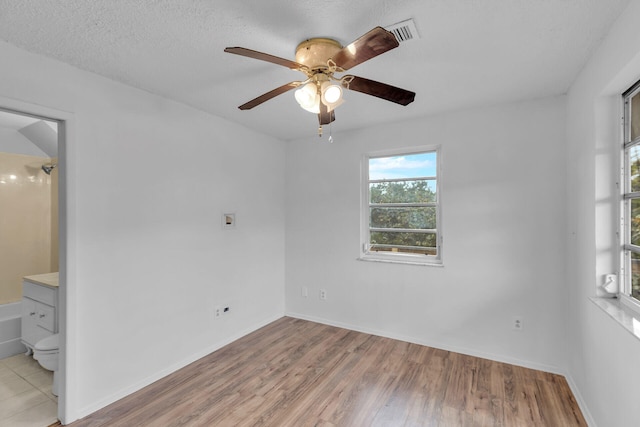 empty room with visible vents, light wood-style floors, ceiling fan, a textured ceiling, and baseboards