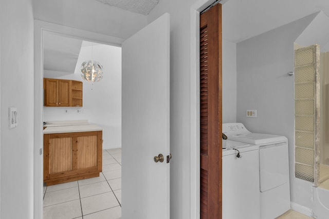 clothes washing area with laundry area, light tile patterned flooring, washing machine and clothes dryer, and an inviting chandelier