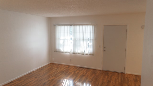 empty room with a textured ceiling and dark hardwood / wood-style flooring