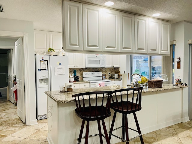 kitchen featuring white appliances, a textured ceiling, light stone counters, and white cabinets