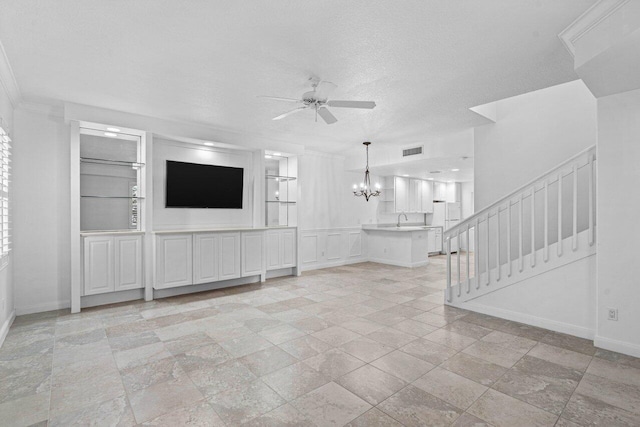 unfurnished living room featuring a textured ceiling, ceiling fan with notable chandelier, visible vents, baseboards, and stairs