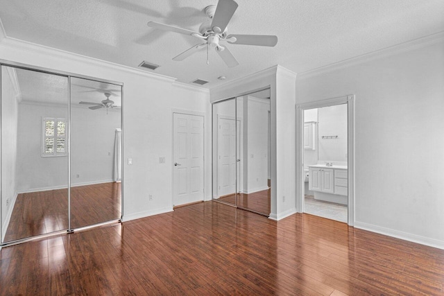 unfurnished bedroom with a textured ceiling, wood finished floors, visible vents, two closets, and crown molding