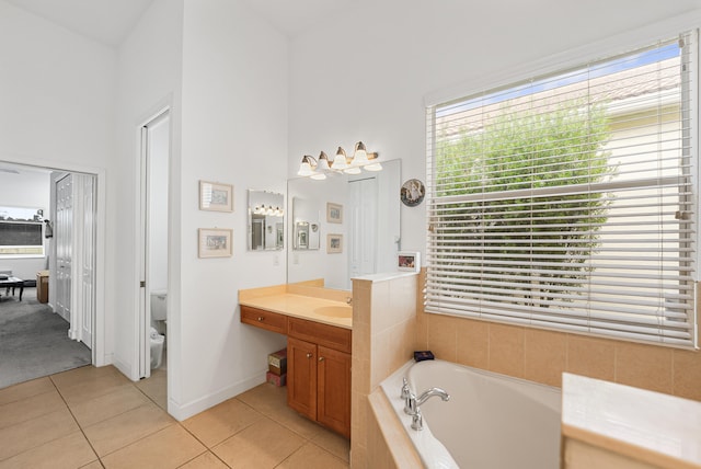 bathroom featuring tile patterned flooring, tiled tub, a towering ceiling, toilet, and vanity