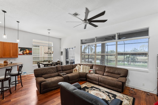 living room featuring a textured ceiling, ceiling fan with notable chandelier, a healthy amount of sunlight, and dark wood-type flooring