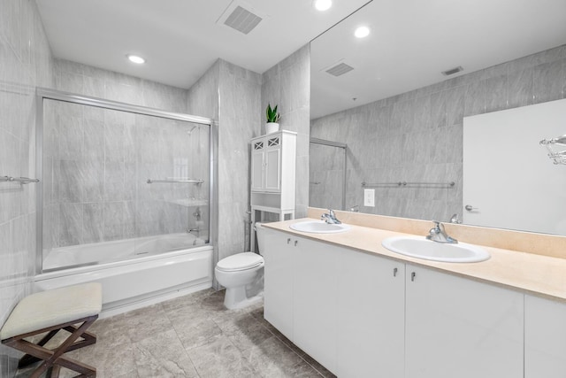 full bathroom featuring toilet, vanity, shower / bath combination with glass door, and tile walls