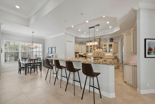 kitchen featuring a spacious island, glass insert cabinets, light stone counters, a tray ceiling, and pendant lighting