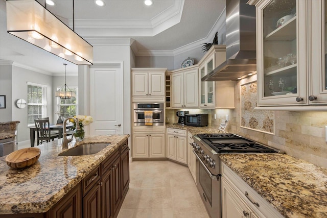 kitchen with stainless steel appliances, a sink, hanging light fixtures, wall chimney range hood, and glass insert cabinets