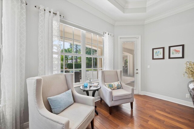 living area with a tray ceiling, ornamental molding, wood finished floors, and baseboards