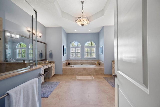 bathroom with tile patterned flooring, a raised ceiling, a garden tub, and vanity