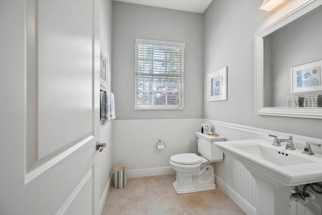 half bathroom with a wainscoted wall, a sink, and toilet