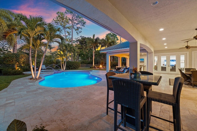 pool at dusk with a patio area, outdoor dining space, a ceiling fan, and french doors