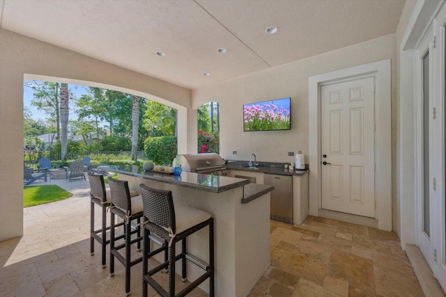 kitchen with refrigerator, stone tile floors, a sink, dark countertops, and a kitchen bar