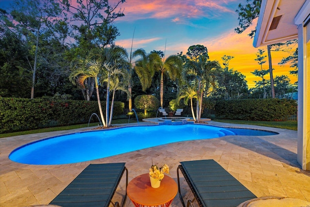 pool at dusk with a pool with connected hot tub, a fenced backyard, and a patio