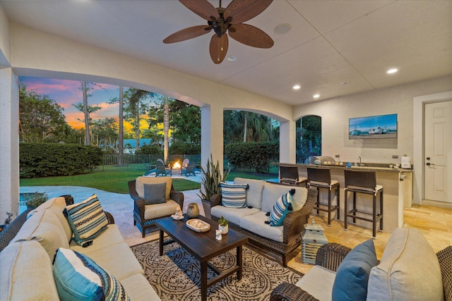 patio terrace at dusk featuring exterior bar, ceiling fan, and an outdoor hangout area