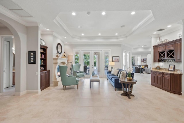 living area with a tray ceiling, french doors, a dry bar, visible vents, and a lit fireplace