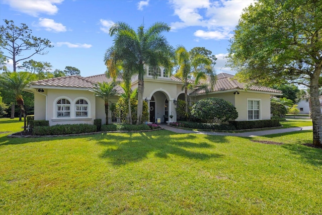 mediterranean / spanish-style home featuring a tile roof, a front lawn, and stucco siding