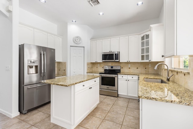 kitchen featuring stainless steel appliances, light stone counters, a center island, sink, and white cabinetry