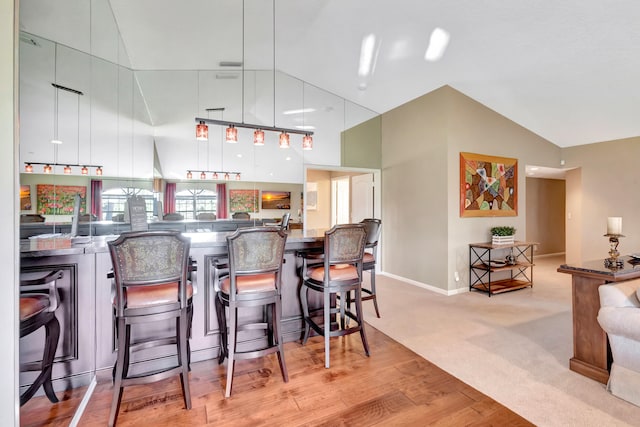 kitchen with a kitchen bar, high vaulted ceiling, light hardwood / wood-style flooring, and decorative light fixtures