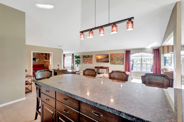 kitchen featuring dark stone countertops, a kitchen bar, hanging light fixtures, and light colored carpet