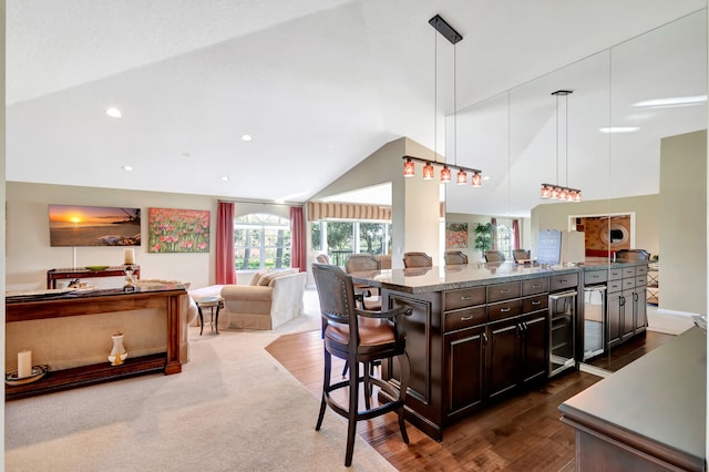 kitchen with a breakfast bar, light stone countertops, decorative light fixtures, dark brown cabinets, and dark wood-type flooring