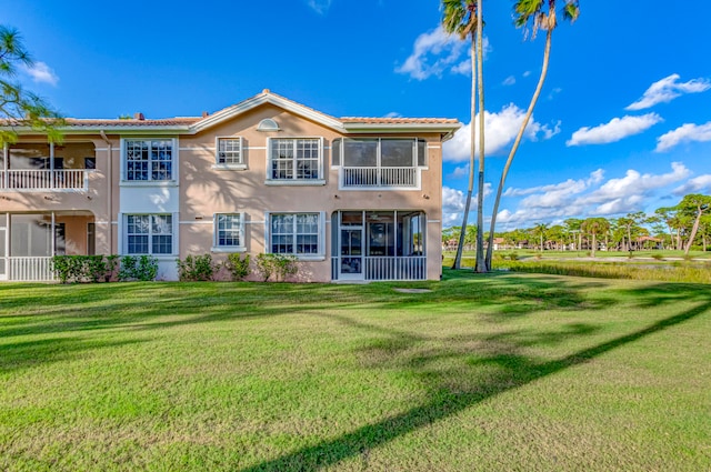 back of property with a balcony, a sunroom, and a yard