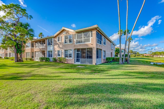 back of property featuring a sunroom, a lawn, and a balcony