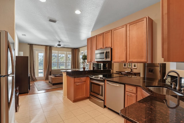 kitchen featuring appliances with stainless steel finishes, a textured ceiling, sink, dark stone countertops, and kitchen peninsula