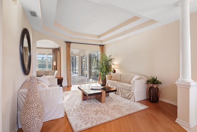 living room featuring ornate columns, a tray ceiling, and light hardwood / wood-style floors