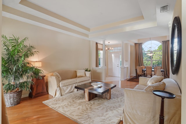 living room featuring ornate columns, a raised ceiling, and light hardwood / wood-style flooring