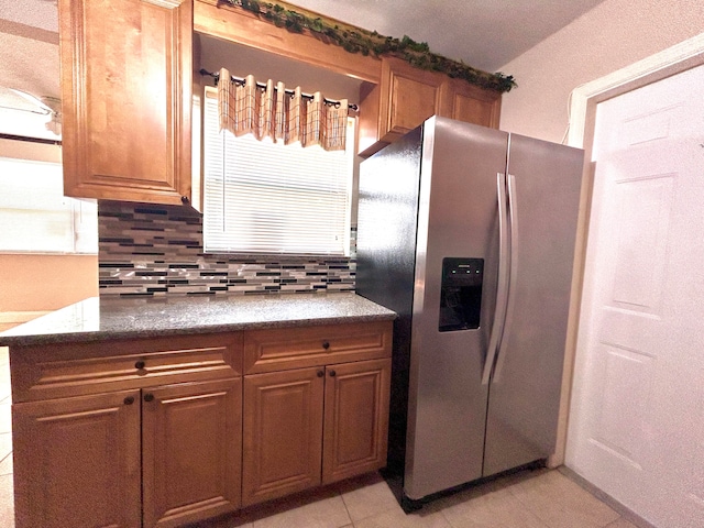 kitchen with light tile patterned floors, tasteful backsplash, dark stone countertops, and stainless steel fridge