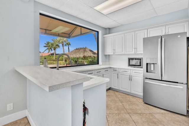 kitchen featuring white cabinetry, stainless steel appliances, light tile patterned flooring, a drop ceiling, and kitchen peninsula