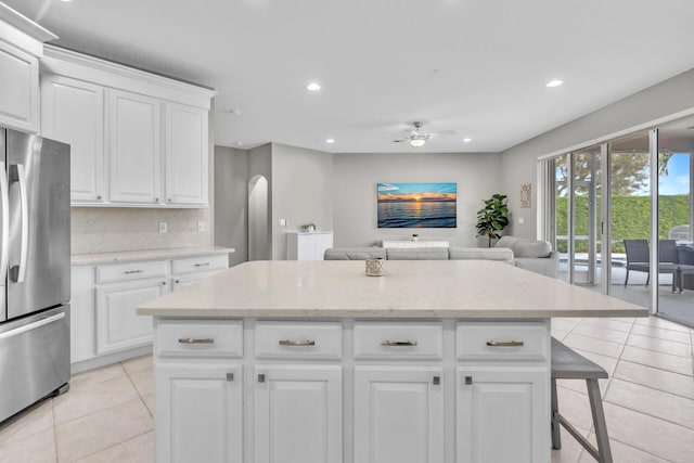 kitchen with a breakfast bar area, stainless steel refrigerator, backsplash, white cabinets, and light tile patterned flooring