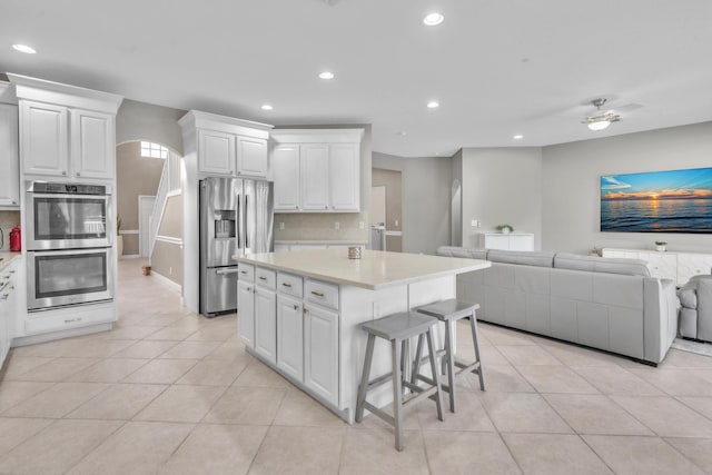 kitchen featuring a kitchen island, appliances with stainless steel finishes, a breakfast bar area, white cabinets, and light tile patterned floors