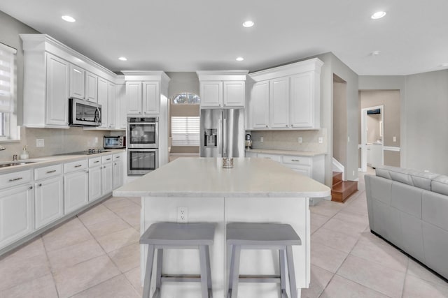 kitchen featuring a kitchen island, white cabinetry, a breakfast bar area, light tile patterned floors, and stainless steel appliances