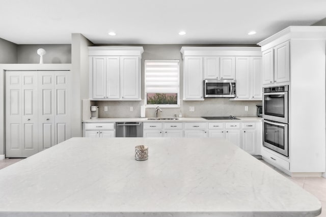 kitchen with sink, light stone counters, white cabinets, stainless steel appliances, and backsplash