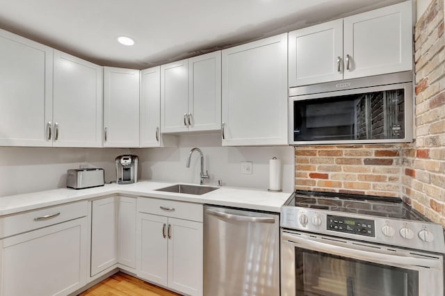 kitchen with white cabinetry, appliances with stainless steel finishes, light stone countertops, and light wood-type flooring