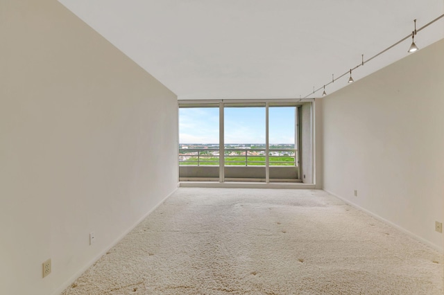 unfurnished room featuring carpet floors, a wall of windows, and rail lighting