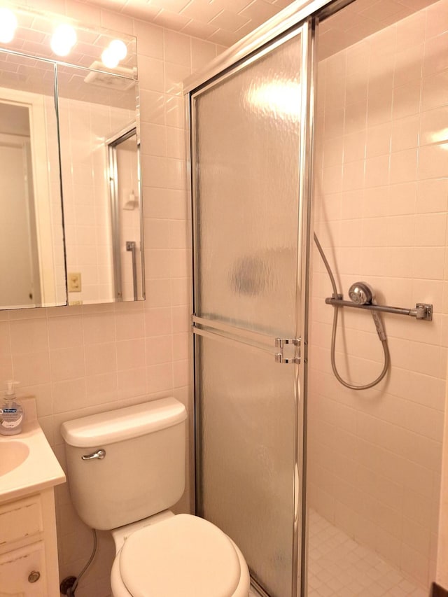 bathroom with walk in shower, vanity, toilet, and tile walls