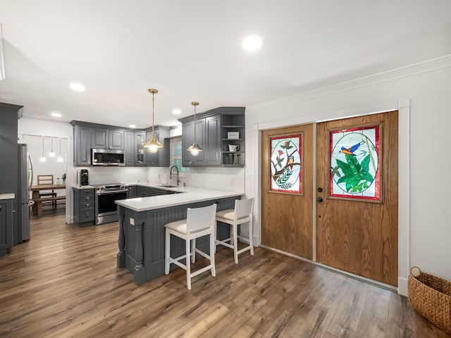 kitchen featuring gray cabinetry, hanging light fixtures, appliances with stainless steel finishes, dark hardwood / wood-style flooring, and kitchen peninsula