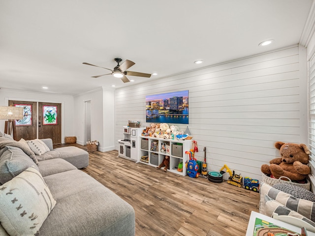 living room featuring wooden walls, light hardwood / wood-style floors, ceiling fan, and crown molding