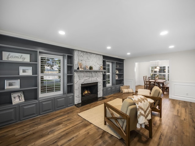 living room featuring a stone fireplace, built in features, dark wood-type flooring, and ornamental molding