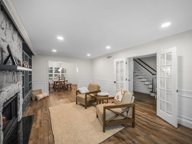 sitting room with french doors, crown molding, dark wood-type flooring, and a stone fireplace