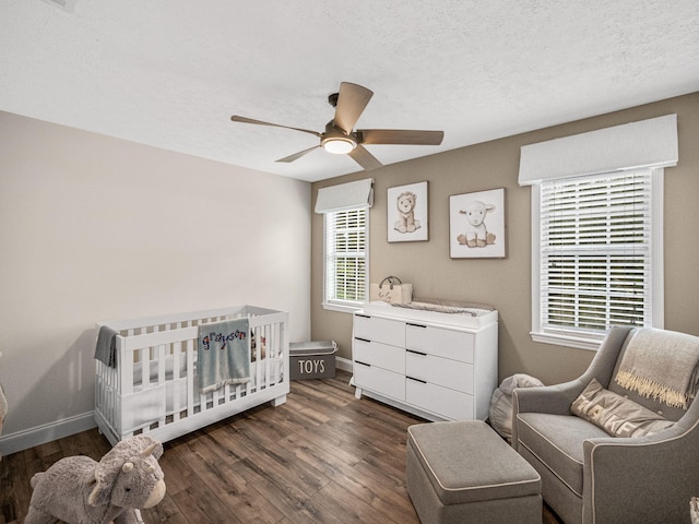 bedroom with a textured ceiling, ceiling fan, dark wood-type flooring, and a crib