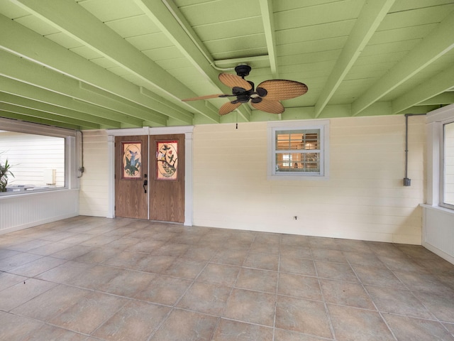 unfurnished sunroom featuring beamed ceiling and ceiling fan