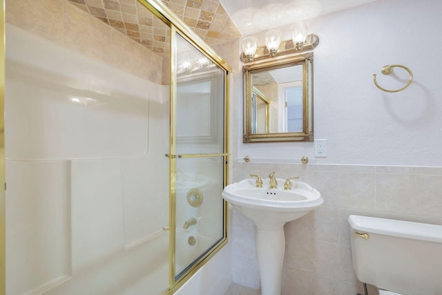 bathroom featuring combined bath / shower with glass door, tile walls, and toilet