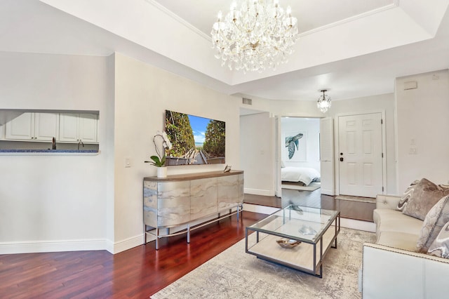 living room featuring a raised ceiling, hardwood / wood-style floors, an inviting chandelier, and ornamental molding