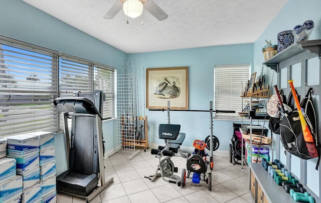 exercise area featuring ceiling fan, light tile patterned flooring, and a textured ceiling